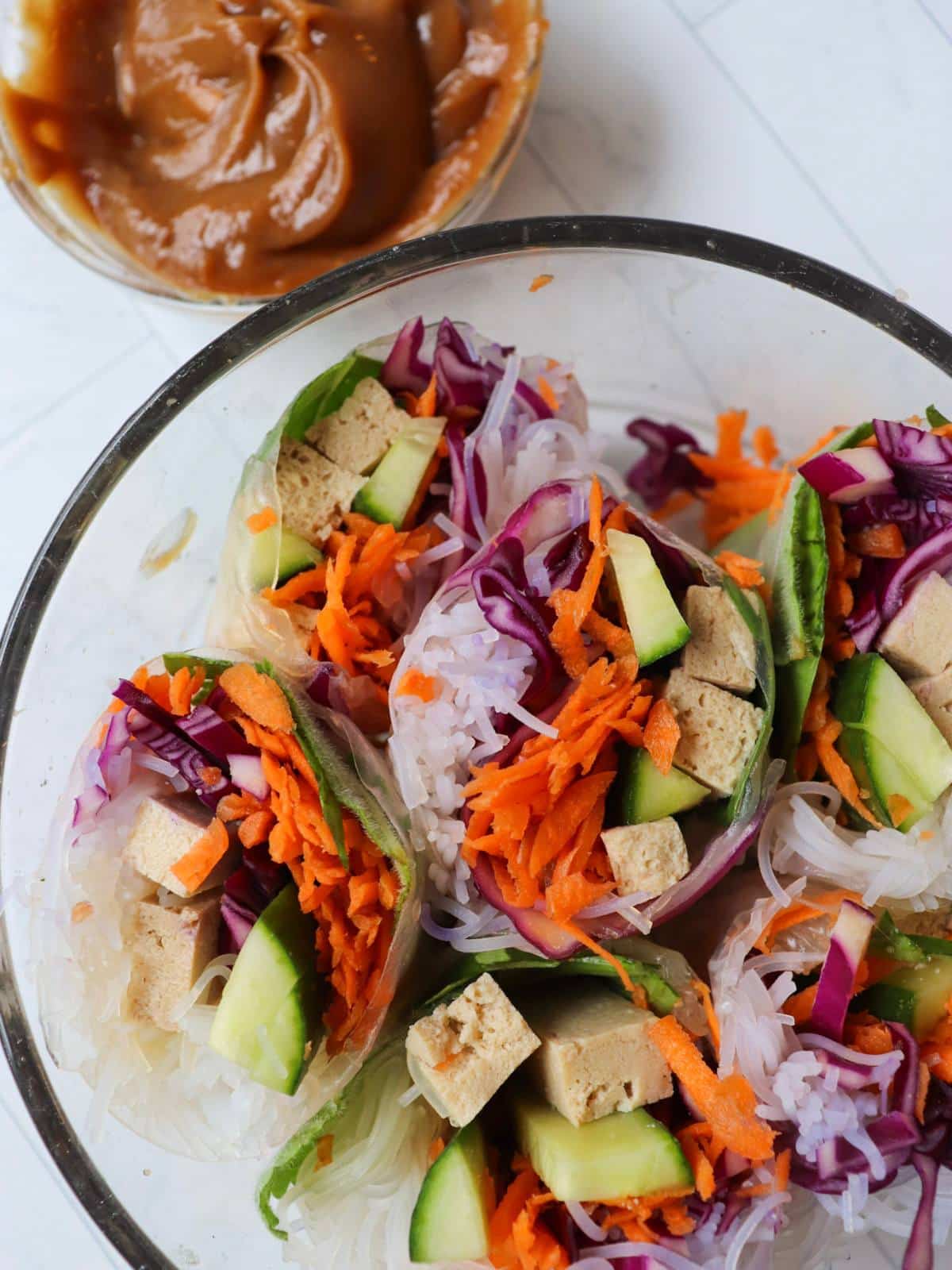 Vegan fresh rolls cut in half and in a bowl next to homemade peanut dipping sauce.