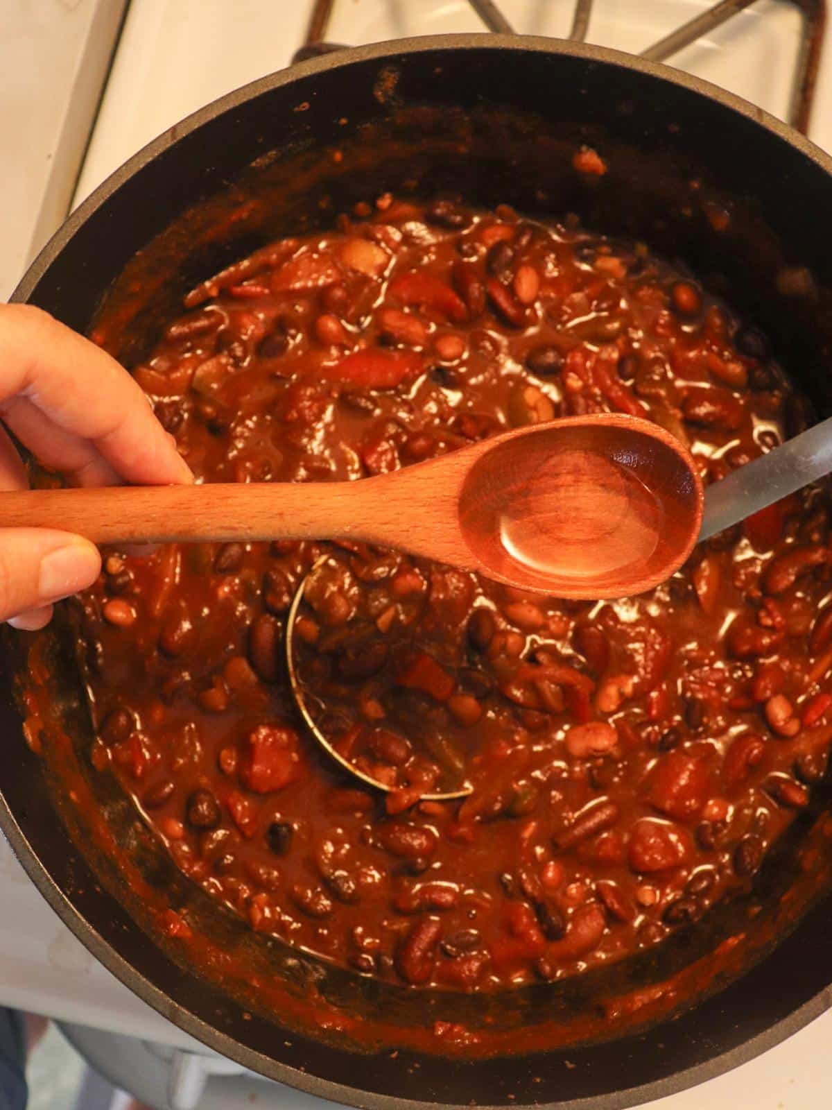 Three bean chili in a dutch oven on the stove with a tablespoon of vinegar getting stirred in.