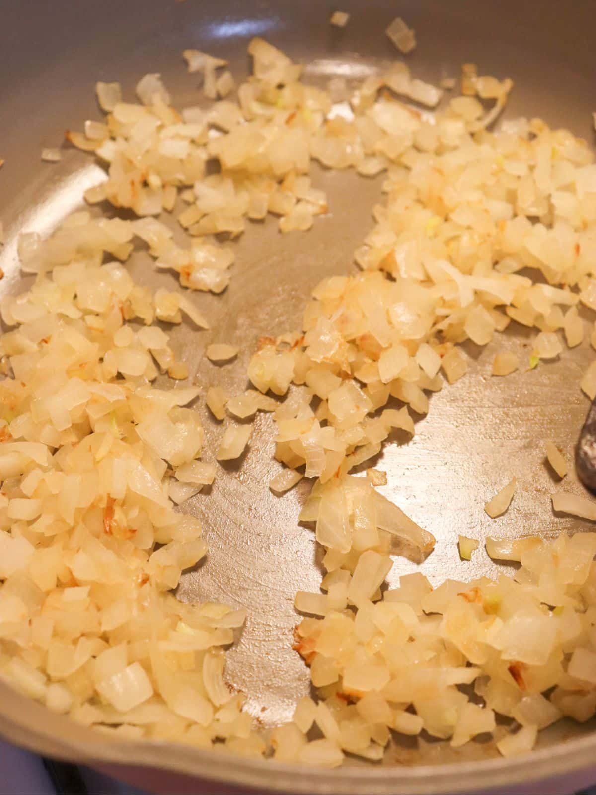 Onions sauteing in a pan on the stove in oil.