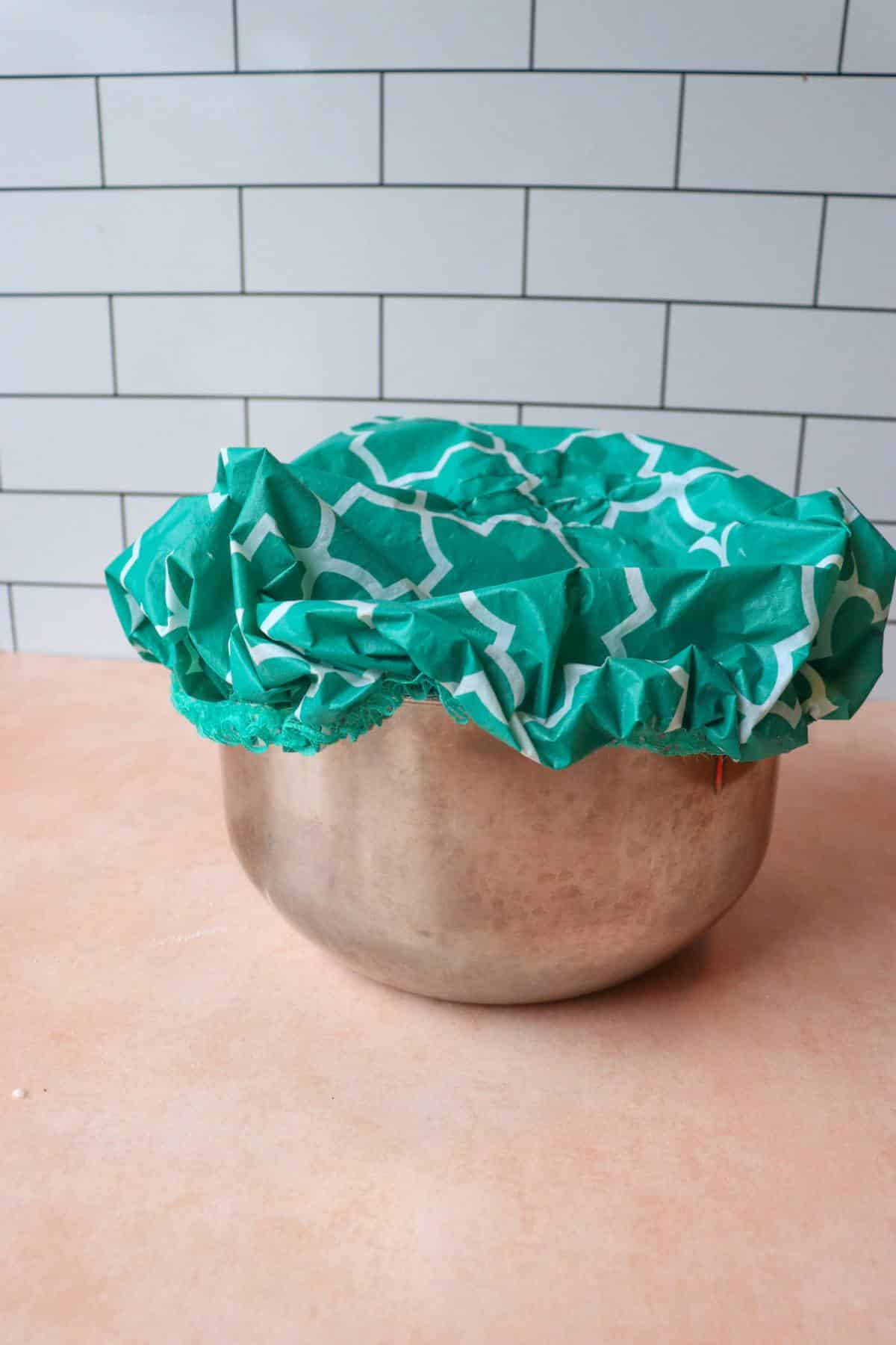 Bread dough in a mixing bowl with a towel covering the bowl.