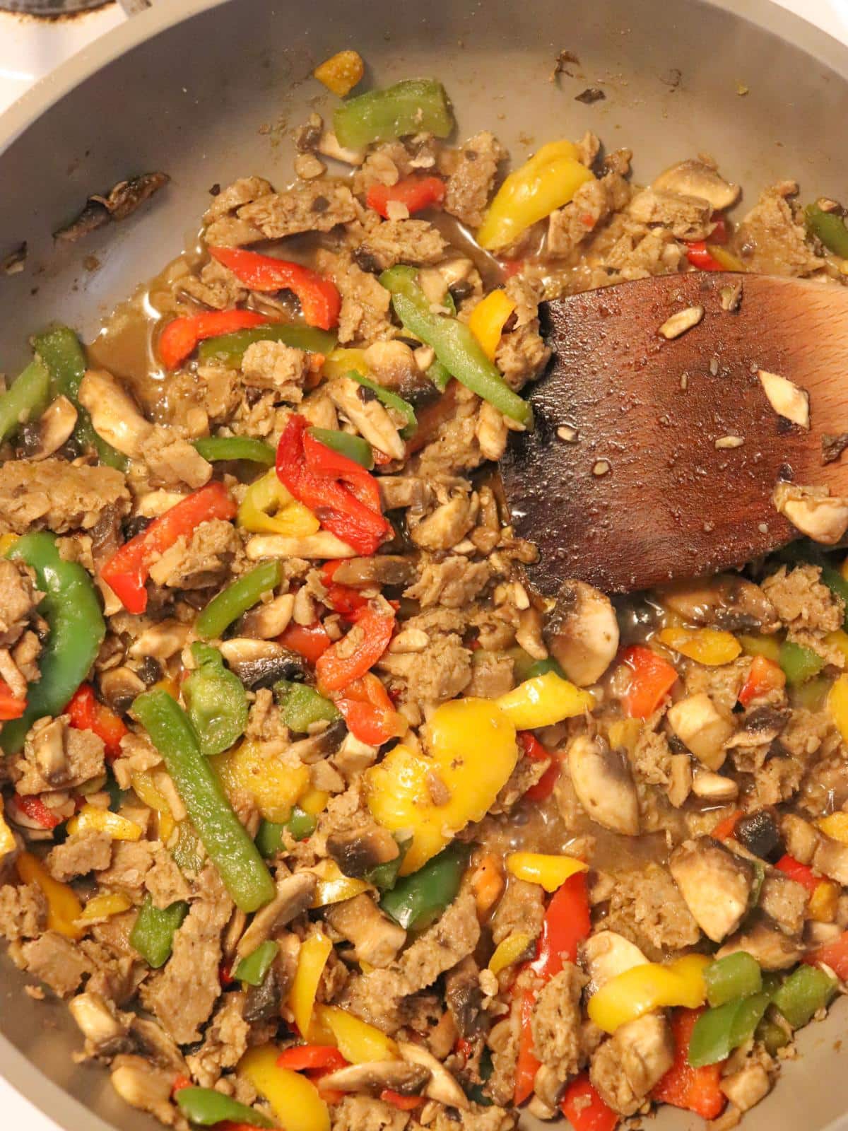 Vegan breakfast sausage, bell peppers and onions sautéing in a frying pan on the stove.
